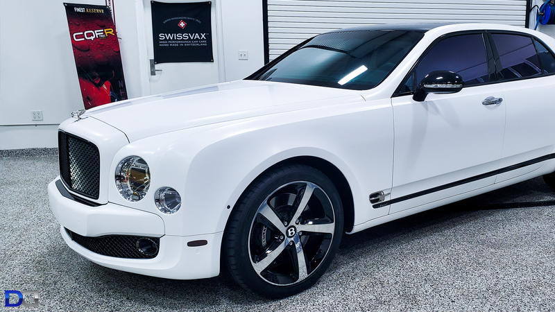 White Bentley with black roof, tinted windows, parked in a shop.