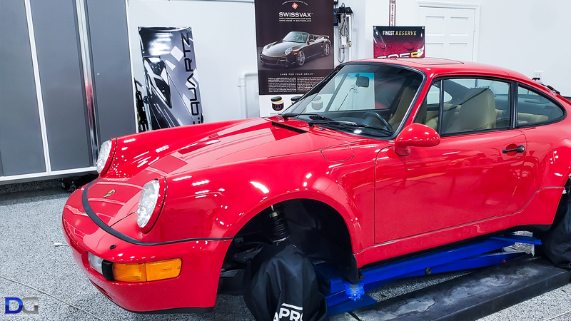 Red Porsche 911 on a lift, wheels removed, in a garage.