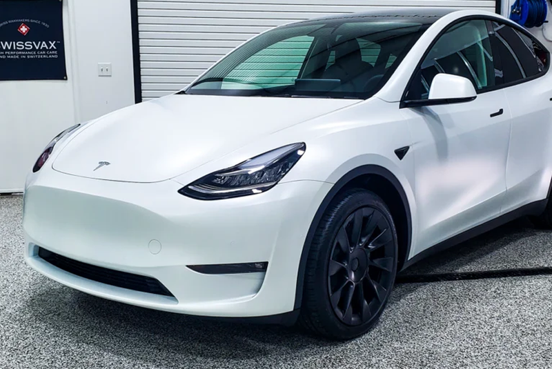 White Tesla Model Y with black wheels parked indoors.