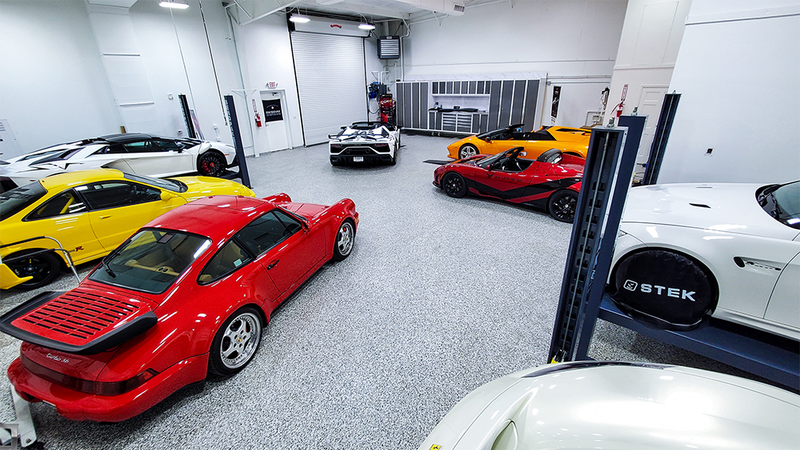 Garage with multiple sports cars in various colors, parked on a speckled floor.