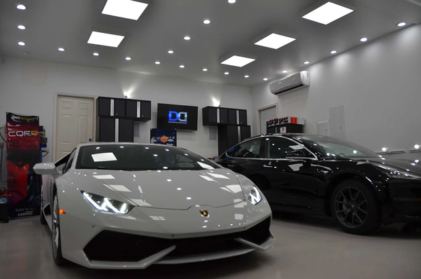 White Lamborghini and black Tesla parked in a modern garage with overhead lighting.