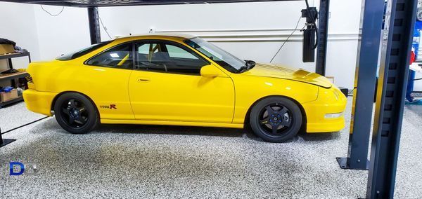 Yellow car on a lift inside a garage. The car has black wheels and a roll cage.