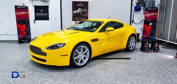 Yellow Aston Martin sports car parked in a garage, with detailing equipment.