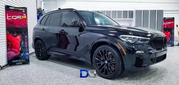 Black BMW SUV in a garage, black wheels, glossy paint, advertising banner.