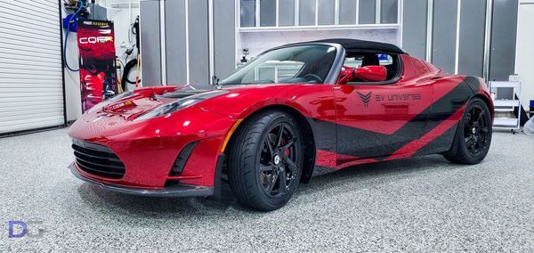 Red Tesla Roadster with black accents in a garage setting.