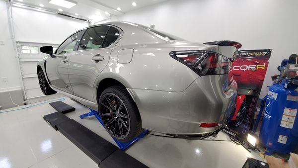 Silver sedan on a lift in a shop, black wheels, spoiler, and equipment nearby.