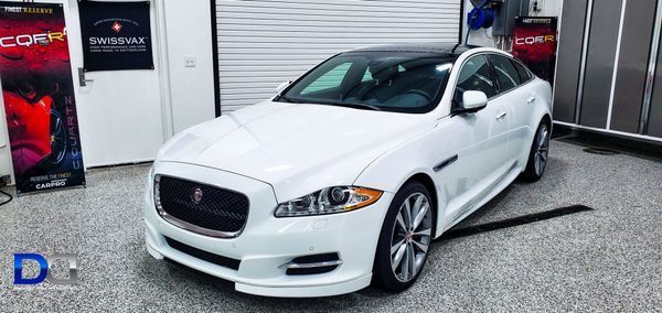 White Jaguar sedan with a black roof in a garage.