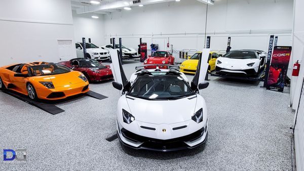 White Lamborghini with open doors, surrounded by other luxury cars in a garage.