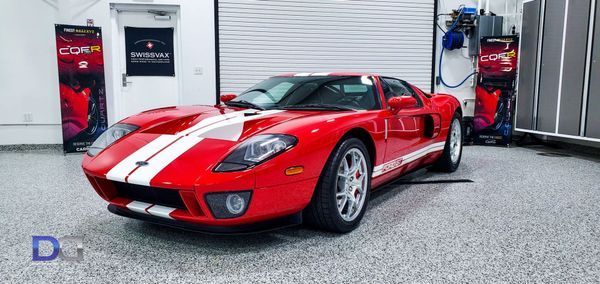 Red Ford GT sports car with white stripes, parked indoors.