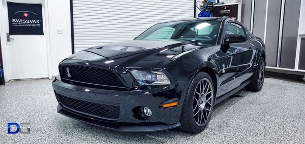 Black Shelby Mustang parked in a garage with a white door and banner.