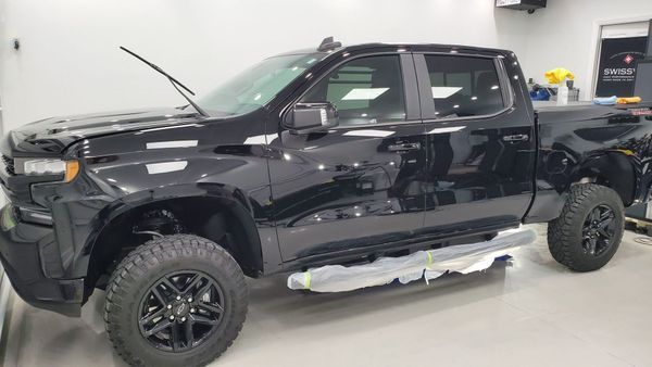 Black Chevrolet Silverado pickup truck in a garage, with tinted windows and black wheels.