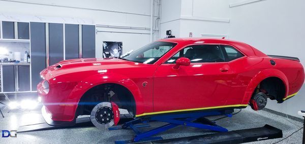 Red Dodge Challenger on a lift in a garage, wheels removed.