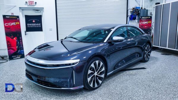 Dark blue Lucid Air electric car parked in a garage, illuminated by overhead lighting.