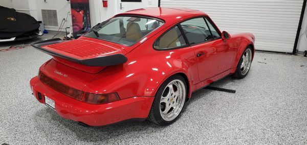 Red Porsche 911 coupe with a black spoiler in a garage with a gray speckled floor.