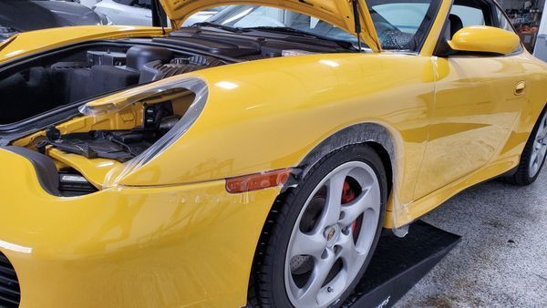 Yellow Porsche with hood up, being worked on, protective film applied to the front.
