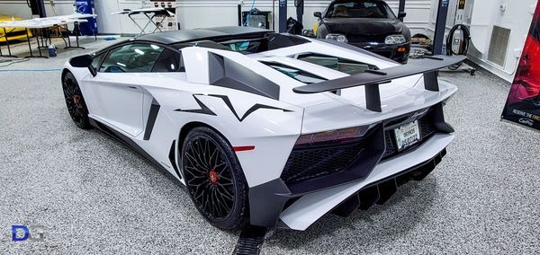 White Lamborghini Aventador SVJ convertible in a garage. Black wheels and spoiler.