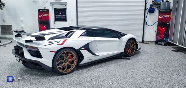 White Lamborghini Aventador SVJ in a garage, black roof and bronze wheels.