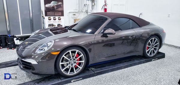 A brown Porsche convertible on a lift in a garage with red brake calipers.