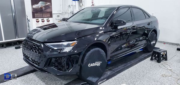 Black Audi sedan on a dynamometer in a garage setting with wheel covers and machinery.