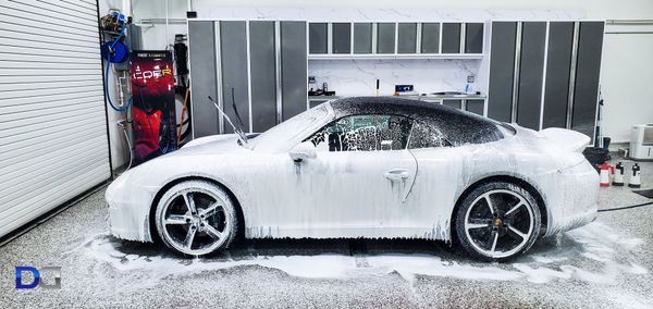 A white sports car covered in white foam, washing it in a garage.