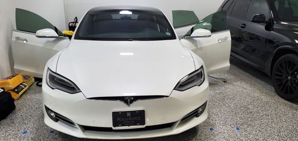 White Tesla with open doors next to a black car in a garage, with tinted windows.