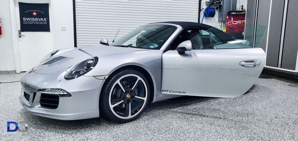 Silver Porsche 911 parked inside a garage. Door is open. Black top with grey interior.