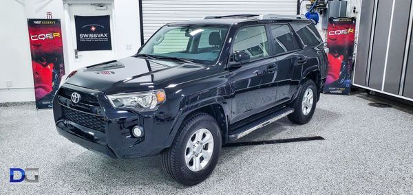 Black Toyota 4Runner parked in a well-lit garage with red and black banners in the background.