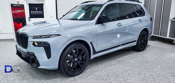 A light gray BMW X7 SUV with black wheels parked inside a garage.