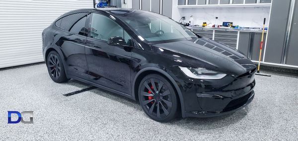 Black Tesla Model X parked in a garage. Black wheels with red calipers.