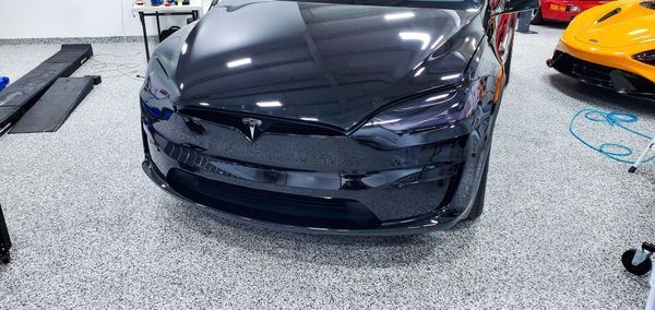 Black Tesla car in a garage, with a yellow sports car in the background.