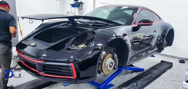 Black Porsche sports car being worked on in a garage, up on a lift.