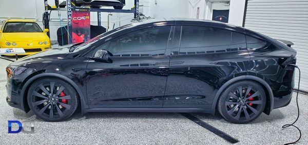 Black Tesla SUV charging in a garage with red brake calipers and tinted windows.