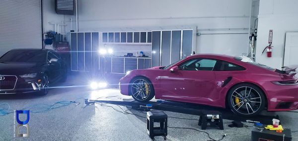 A magenta Porsche on a lift inside a garage next to a black Audi.