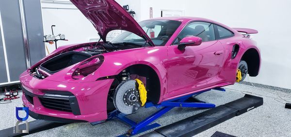 Pink Porsche on a lift with the hood open, in a garage.