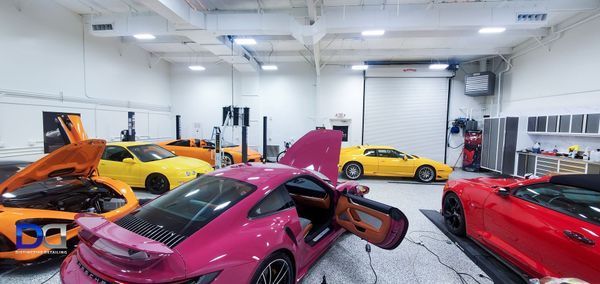Cars in a garage: pink, yellow, orange, and red sports cars with open doors/hoods.