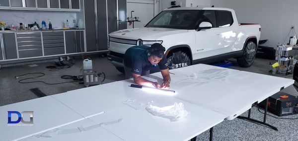 A person cuts something on a white table with a white Rivian truck in the background in a garage.