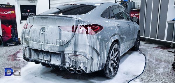 A gray Mercedes SUV covered in soapy foam, undergoing a car wash, indoors.