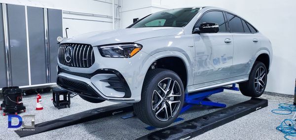 White Mercedes SUV on a lift in a garage. The car is being worked on. Gray cabinets in the background.