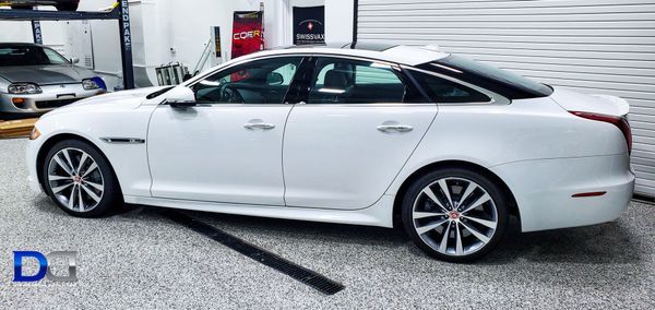 White Jaguar sedan parked in a garage with a silver Supra in the background.