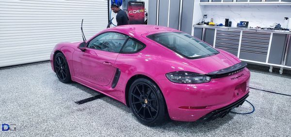 Pink Porsche sports car in a garage, person working on it, black wheels.