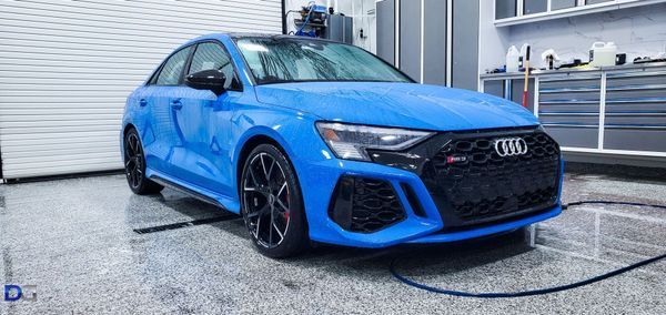 Blue Audi RS3 sedan in a garage with a white door.