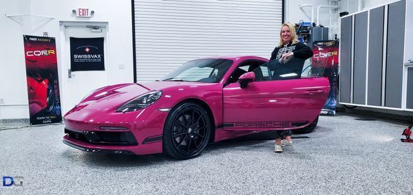 Woman standing next to a pink sports car, door open. Garage setting.