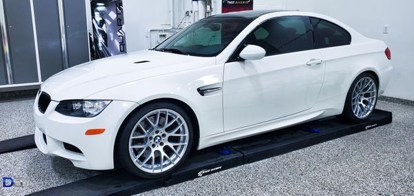 White BMW M3 coupe on a dynamometer, inside a garage.