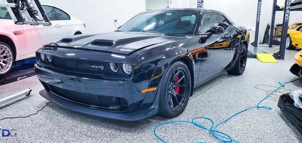 Black Dodge Challenger in a garage with other vehicles.