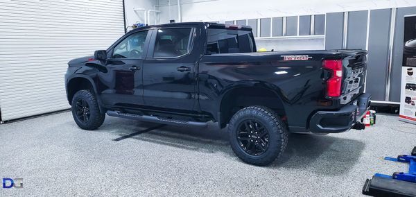 Black pickup truck in a garage, angled to the left.  Black wheels, running board. Bright lights.