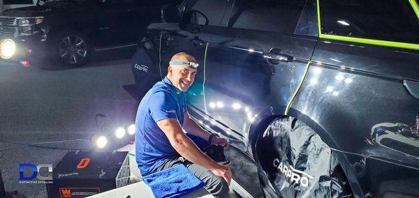 A man in blue shirt polishing a black car under bright lights.
