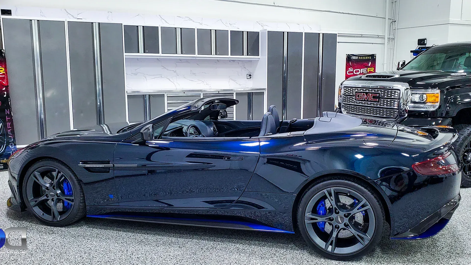 Dark blue convertible sports car on display, blue accents, grey wheels, indoors.