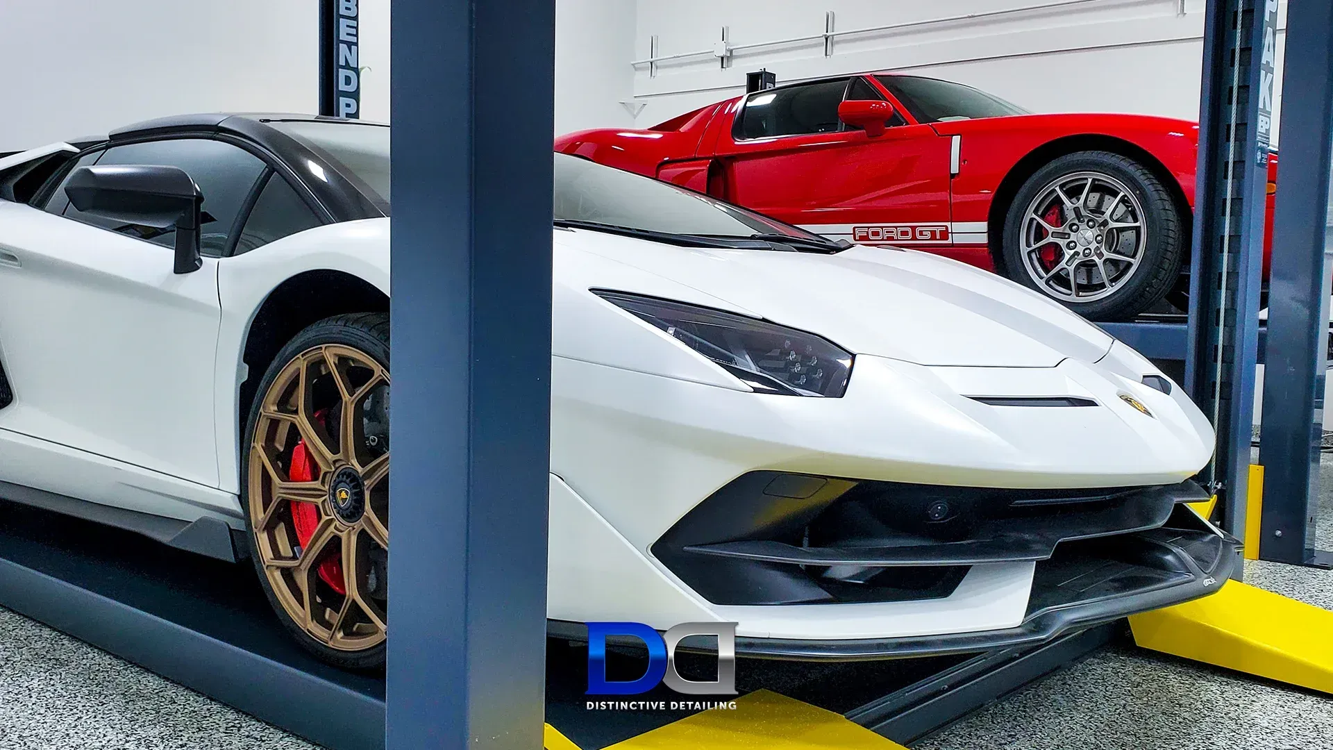 White Lamborghini and red Ford GT sports cars in a garage, one on a lift.