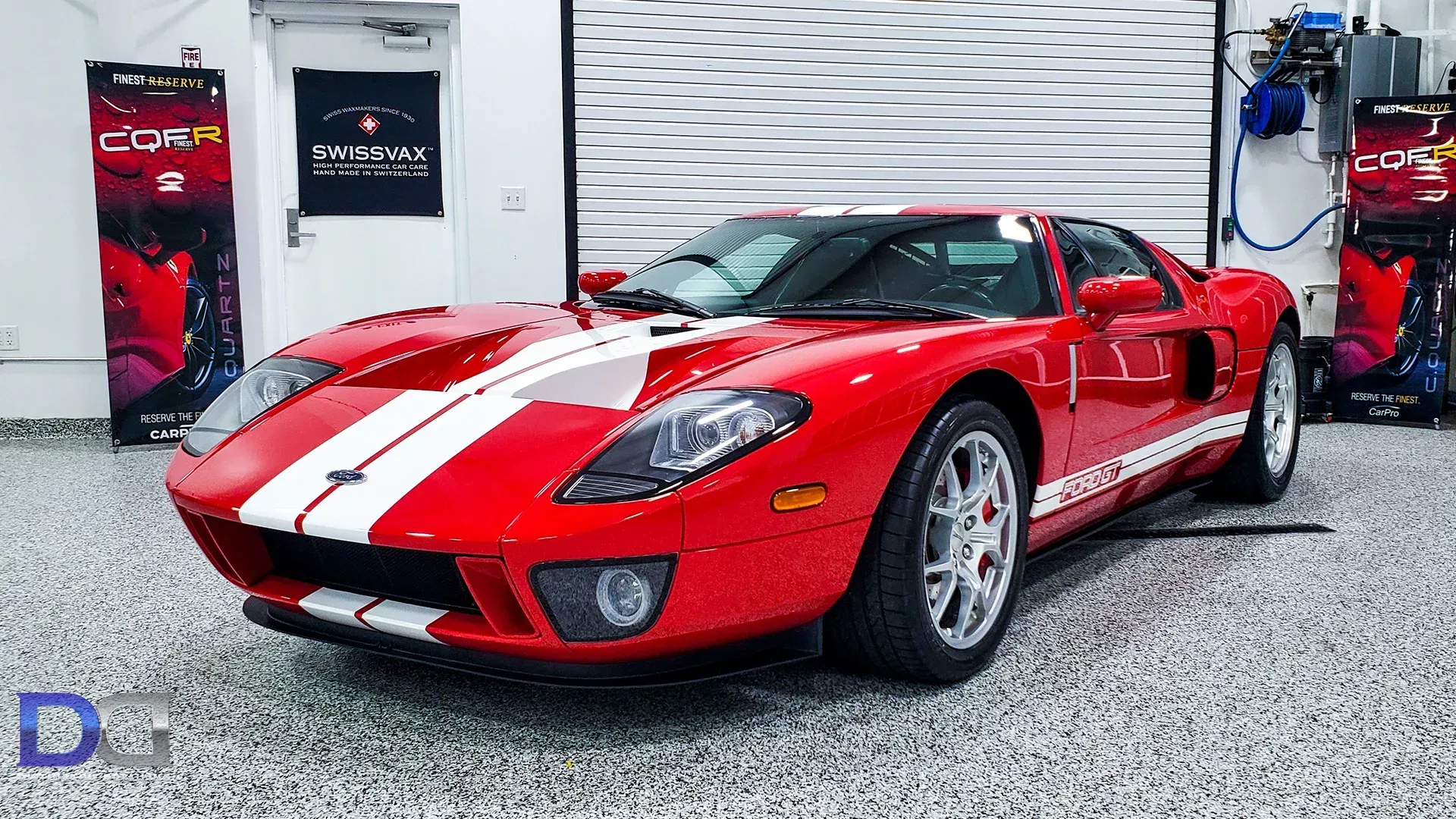Red Ford GT sports car with white racing stripes, indoors.