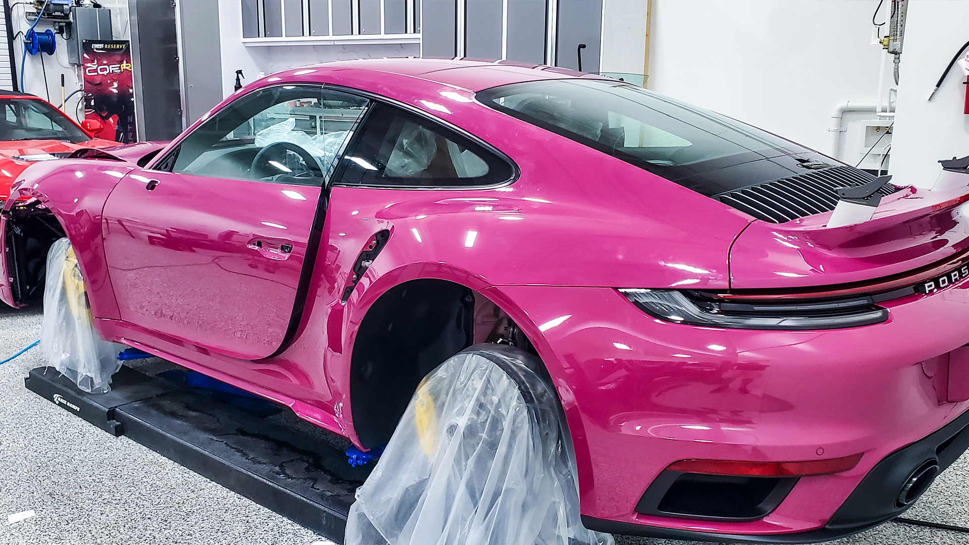 Pink Porsche sports car in a workshop being worked on, covered in protective film.